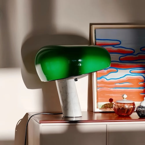 Post-modern marble desk lamp in vibrant green finish on a shelf with artwork in the background.
