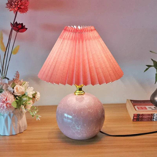 Pink Mushroom Lamp with pleated pink shade on a wooden table, surrounded by flowers and books, adding a whimsical touch to decor.