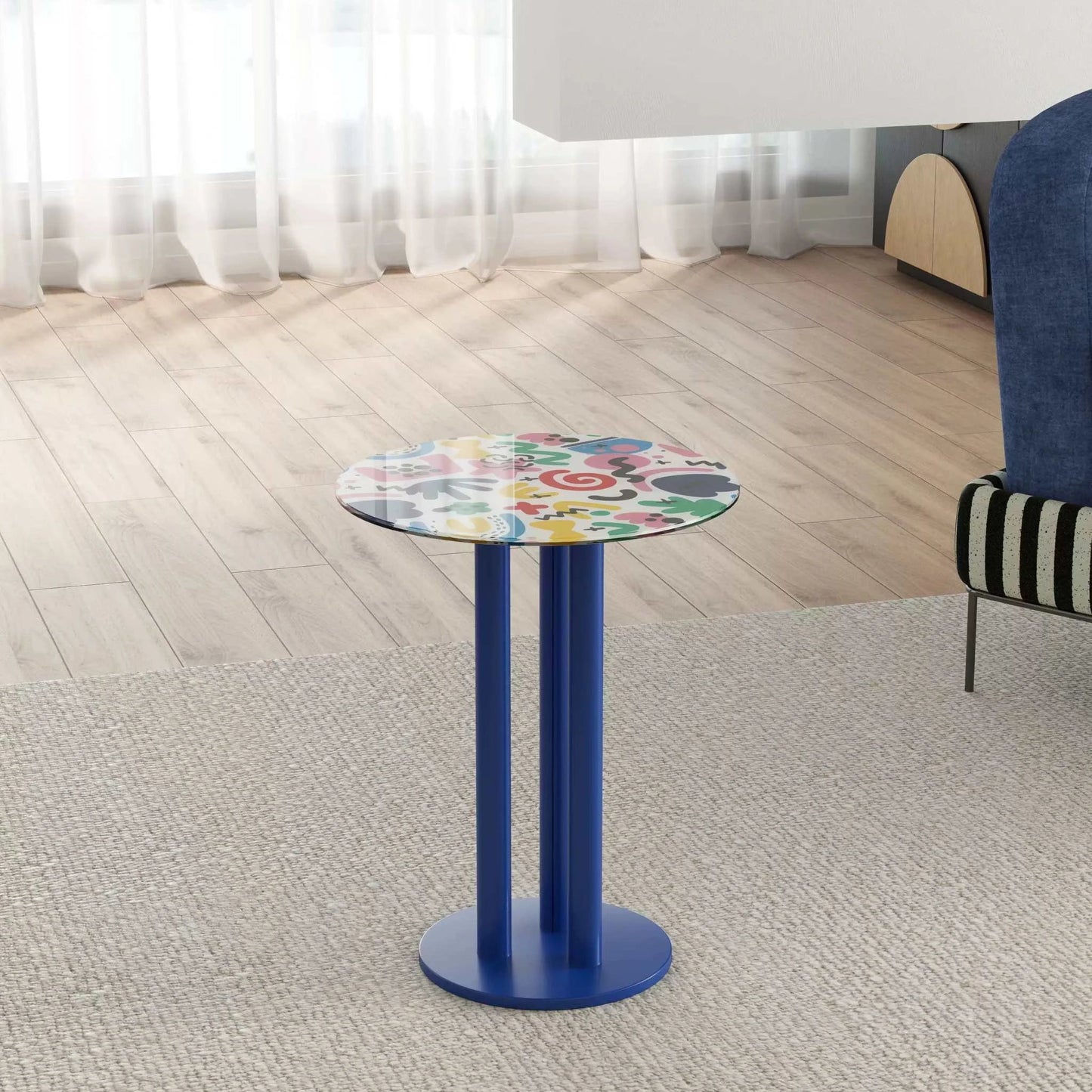 Colorful round table with blue base in a room with light wood flooring and a window.