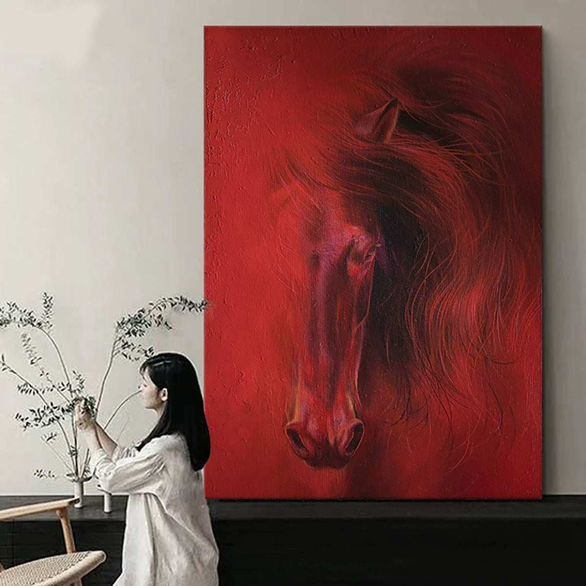 Woman sitting in front of a large red painting of a horse in a room with minimal decor.